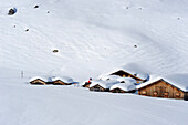 Drei Skitourengeher sitzen auf Dächern von verschneiten Almhütten, Rätikon, Montafon, Vorarlberg, Österreich