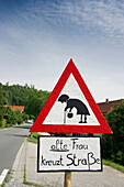 Homemade street sign showing an old woman crossing the road, near Hoeslwang, Bavaria, Germany