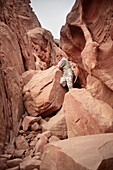 Young man on a rock, demanding hike circumnavigation of the Seven Pillars of Wisdom mountain, Wadi Rum, Jordan, Middle East, Asia