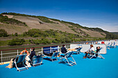 Menschen sonnen sich auf dem Deck von Flusskreuzfahrtschiff MS Bellevue mit Blick auf Weinberge, Rheinland-Pfalz, Deutschland, Europa