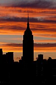 The Empire State Building and other Manhattan buildings are silhouetted against orange colored clouds shortly before sunrise, New York City, New York, USA