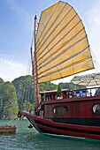 Traditional style cruising junk with hoisted sail moored among islands of Halong Bay Vietnam