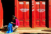 Nepal a woman is sewing a blue dress in front of a red dentist shop