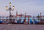 Traditional gondolas moored along the waterfront in Venice, looking towards the island of Church of San Giorgio Maggiore. Dawn.