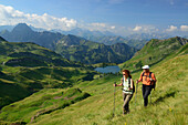 Two hikers in front of lake Seealpsee and Hoefats, trail from Nebelhorn to Laufbacher Eck, Allgaeu range, Upper Allgaeu, Allgaeu, Swabia, Bavaria, Germany