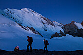 Ein Mann und eine Frau beim Wandern mit Stirnlampe im Aufstieg in der Morgendämmerung zum Wandergipfel der Wilden Frau, Blick zum Blüemlisalpmassif, Blüemlisalphorn, Berner Oberland, Kanton Bern, Schweiz