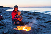 Mutter und Sohn (2 Jahre) sitzen an einem Lagerfeuer am Strand, Schaabe, Insel Rügen, Mecklenburg-Vorpommern, Deutschland