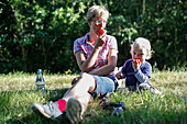 Mother and son (2 years) sitzing on a meadow while eating tomatos, Haide, Ummanz, Island of Ruegen, Mecklenburg-Western Pomerania, Germany