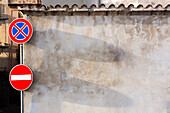 Two traffic signs on a wall in the town of Bosa. A stop sign and a no parking sign.