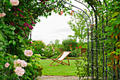 A country garden with a rose arch, and flowering climbing roses.