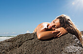 A woman in a bikini laying her head on a rock along the coast, gold coast queensland australia