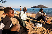 A boy, an old man and a young man sitting on the beach of Lake Malawi and repairing fishing nets, Chembe Village, Cape Mclear, Malawi, Africa