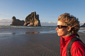 blocked for illustrated books in Germany, Austria, Switzerland: Woman on the beach on a windy day, Archway Islands in the background, Wharariki Beach, South Island, New Zealand