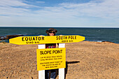 Woman behind a sign showing the southernmost point of South Island, Slope Point, Catlins, South Island, New Zealand