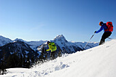 Two backcountry skiers downill skiing from mount Brechhorn, Grosser Rettenstein in background, Kitzbuehel Alps, Tyrol, Austria