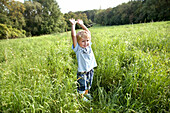 Junge (3 Jahre) steht im Gras und streckt sich, Wien, Österreich