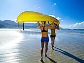 Hawaii, Kauai, Hanalei Bay, Two active young woman carrying a kayak into the ocean.