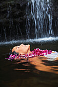 Hawaii, Oahu, Manoa Falls, Beautiful female with orchids leis floating at the bottom of Manoa Waterfalls.