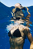 Hawaii, Big Island, Honaunau Bay, Young woman breaking ocean surface while swimming.