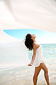 Hawaii, Oahu, Lanikai, Beautiful young woman on beach with white fabric blowing in the wind.