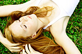 Young woman with freckles and red hair lays in the grass.