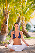 Hawaii, Woman meditating on beach among palm trees.