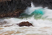 Hawaii, Maui, Makena, An ocean wave crashes among a lava coast.