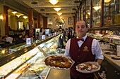 Waiter with traditional Bolo Rei cakes at Pastelaria Versailles cafe and bakery in Saldanha district, Lisbon, Lisboa, Portugal