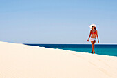 Young woman with hat walking along a sand dune, Playa de Sotavento, Sotavento, Costa Calma, Jandia, Morro Jable, Fuerteventura, Canary Islands, Spain, Europe