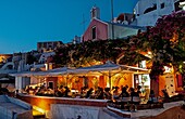Night exposure after sunset of warm restaurant with tourists on cliff of beautiful Oia in Santorini Greece in Greek Islands