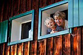 Mother and son (2 years) looking out of a window of an alpine hut, near Maria Alm, Pinzgau, Salzburg, Austria