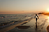 Surfer läuft den Strand entlang bei Sonnenuntergang, Castiglione della Pescaia, Mittelmeer, Provinz Grosseto, Toskana, Italien, Europa