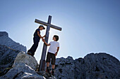 Zwei Jungen reichen sich am Gipfelkreuz die Hände