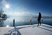 Mann steht auf einem verschneiten Steg am Kochelsee, Oberbayern, Deutschland