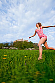 Junge Frau läuft über eine Wiese, Riegersburg im Hintergrund, Steiermark. Österreich