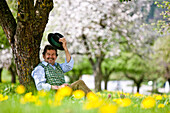 Mann sitzt in einem blühenden Obstgarten, Stubenberg, Steierermark, Österreich