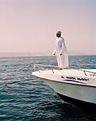 OMAN, Muscat, man standing on deck of boat in traditional clothing at sea
