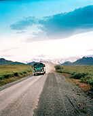 USA, Alaska, Denali National Park, tourist bus on road with snow capped mountains in background