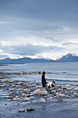 ALASKA, Homer, kids play by the edge of Kachemak Bay at Bishop Beach with the Kenai Mountains in the distance