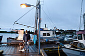 ALASKA, Sitka, fisherman Bill Dorn and his dog Baranof on the dock by an old fishing boat in the Sitka Harbor