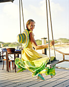 Aruba, Surfside Marina, a young woman sits on a swing smiling at Pinchos Bar & Grill