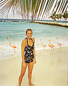 ARUBA, portrait of young woman standing on the beach smiling in the middle of Pink Flamingos, Renaissance Island