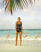 ARUBA, portrait of young woman standing on the beach smiling in the middle of Pink Flamingos, Renaissance Island