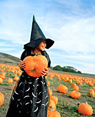 USA, California, young girl dressed as a witch holding a pumpkin, Half Moon Bay