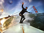 USA, California, San Francisco, Fort Point, surfer on a wave at Fort Ponit Surf Break in front of the Golden Gate Bridge, Sunset