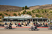 USA, California, Malibu, bikers ride past the front of Neptunes Net Restaurant on the Pacific Coast Highway, the Malibu hills in the distance