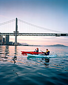 USA, California, San Francisco, a man and woman kayak in the San Francisco Bay under the Bay Bridge, the city of San Francisco in the distance