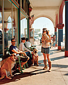 USA, California, Venice Beach, Los Angeles, a young woman and her friends gather in front of the Cafe Collage on the corner of Pacific Avenue and Windward Avenue