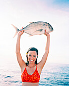 FIJI, Northern Lau Islands, a smiling young woman holds up a travail fish