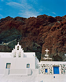 GREECE, Santorini, Akrotiri, white chapel with blue doors against the red rock at Red Sand Beach
